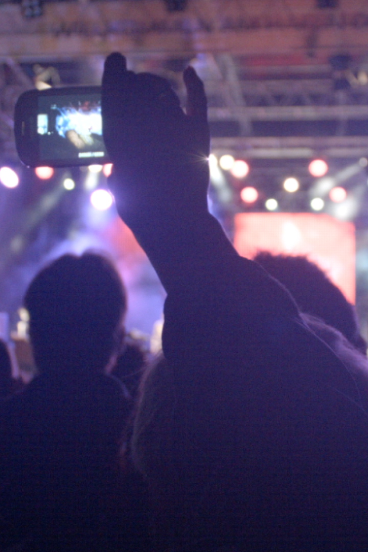 Eine Menschenmenge besucht ein Konzert, eine Person filmt die Bühne mit ihrem Smartphone.