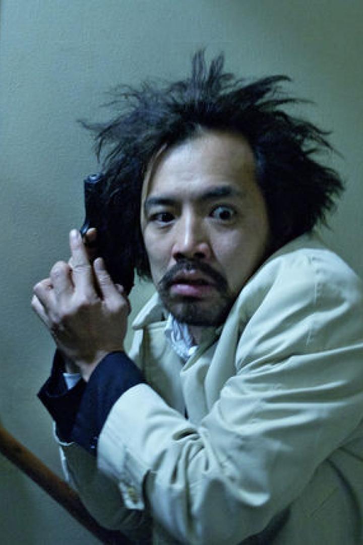 Ein Mann mit wirren Haaren zielt mit einer Pistole.