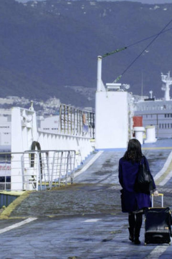 Eine Frau geht mit einem Rollkoffer auf dem Deck einer Fähre.