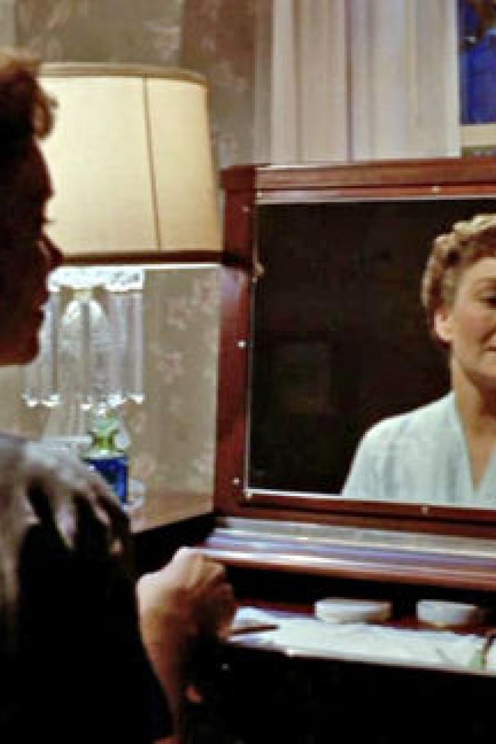 Eine Frau betrachtet ihr Spiegelbild an einem Schminktisch.