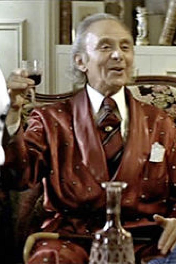 Drei Männer sitzen in einem Raum, einer hält ein Weinglas in der Hand.