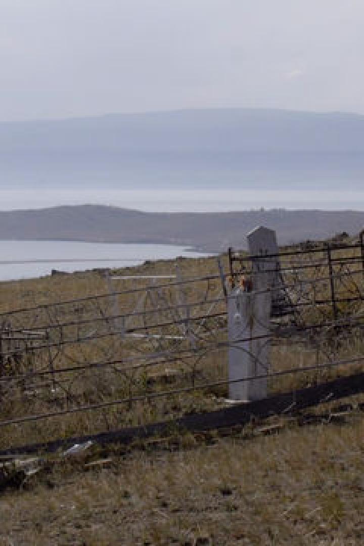 Ein Friedhof auf einem Hügel mit Blick auf einen See und Berge im Hintergrund.