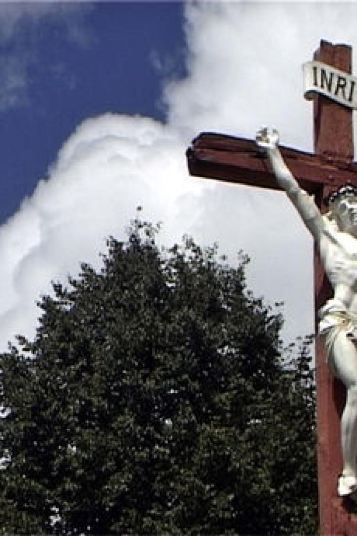 Eine Christusstatue an einem Holzkreuz unter blauem Himmel mit Wolken.