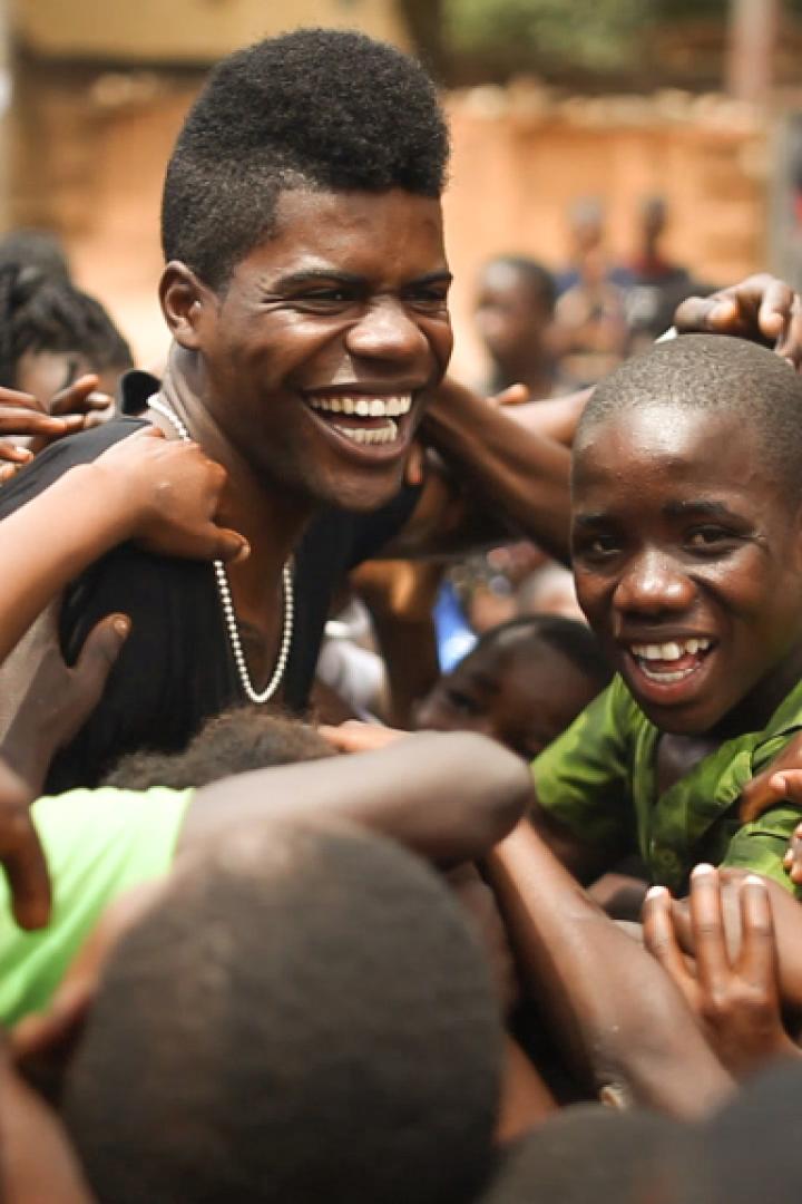 Ein lachender Mann wird von einer Gruppe aufgeregter Kinder umringt.