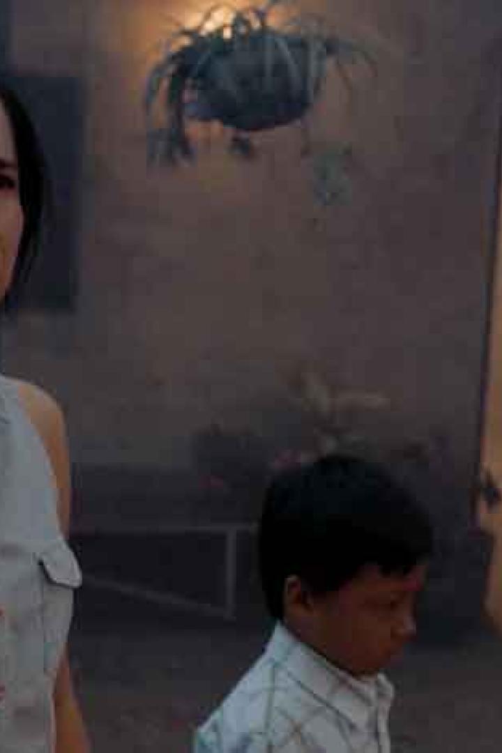 Eine besorgte Frau steht mit einem kleinen Jungen vor einem Haus.