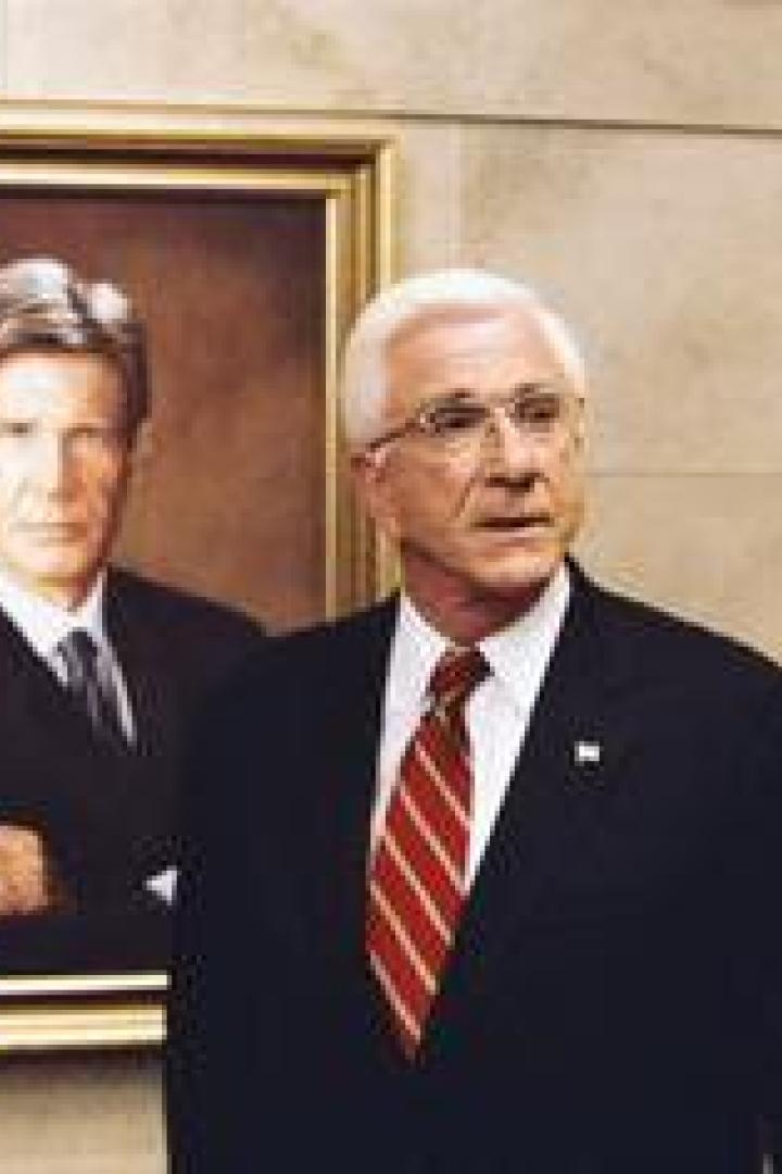 Ein Mann mit weißem Haar steht vor einem Porträt von Harrison Ford.