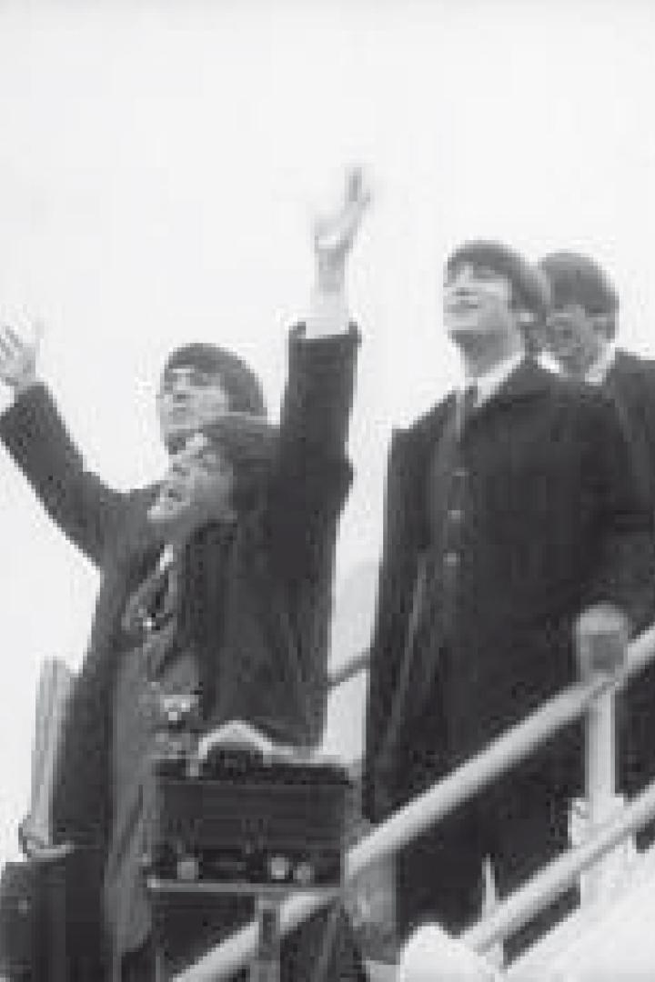 Die Beatles steigen eine Flugzeugtreppe hinunter und winken.