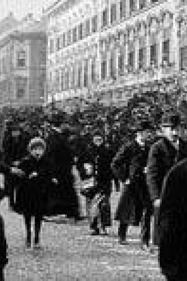 Eine Menschenmenge geht eine belebte Straße entlang, viele tragen Hüte.