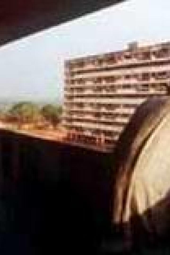 Ein Mann steht auf einem Balkon und blickt auf ein Hochhaus und die Landschaft.