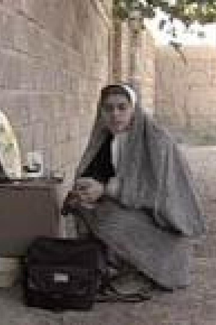 Eine junge Frau kauert neben einer Mauer mit einem kleinen Tisch und einer Tasche.