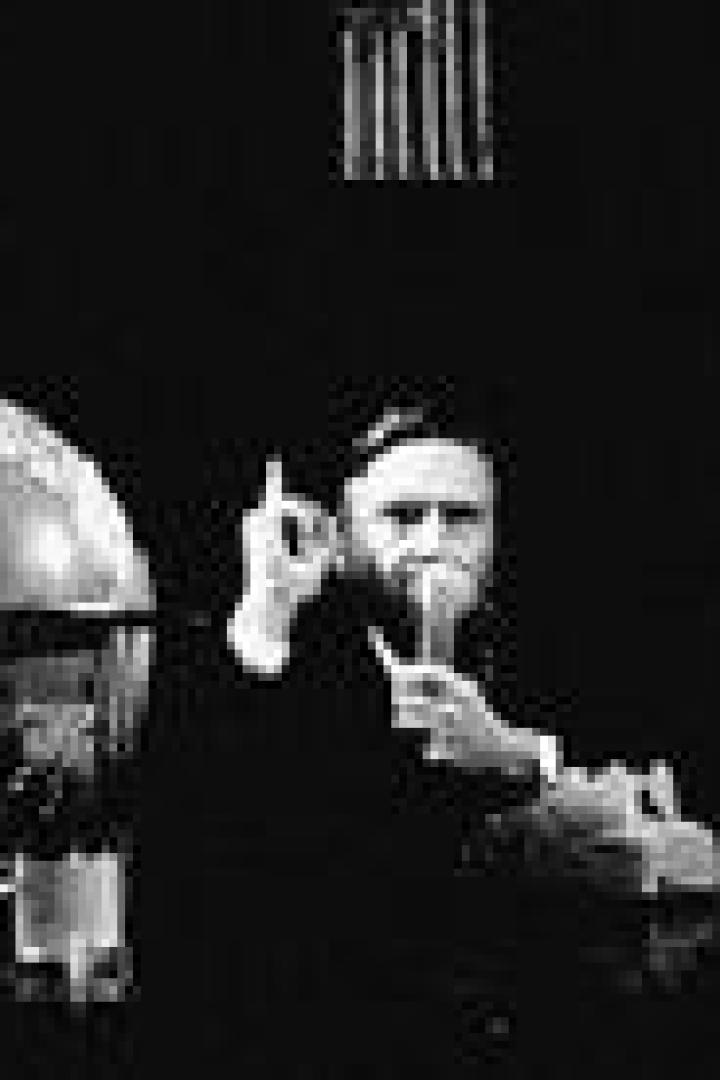 Ein Mann mit Bart sitzt an einem Tisch mit einem Globus und hält ein Glas in der Hand.