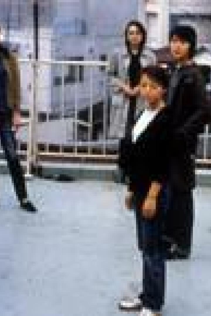 Eine Gruppe von sechs Personen steht auf einer Dachterrasse vor einer Stadtkulisse.