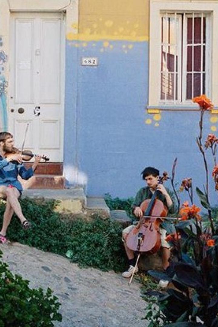 Zwei Musiker spielen Geige und Cello vor einem farbenfrohen Haus.
