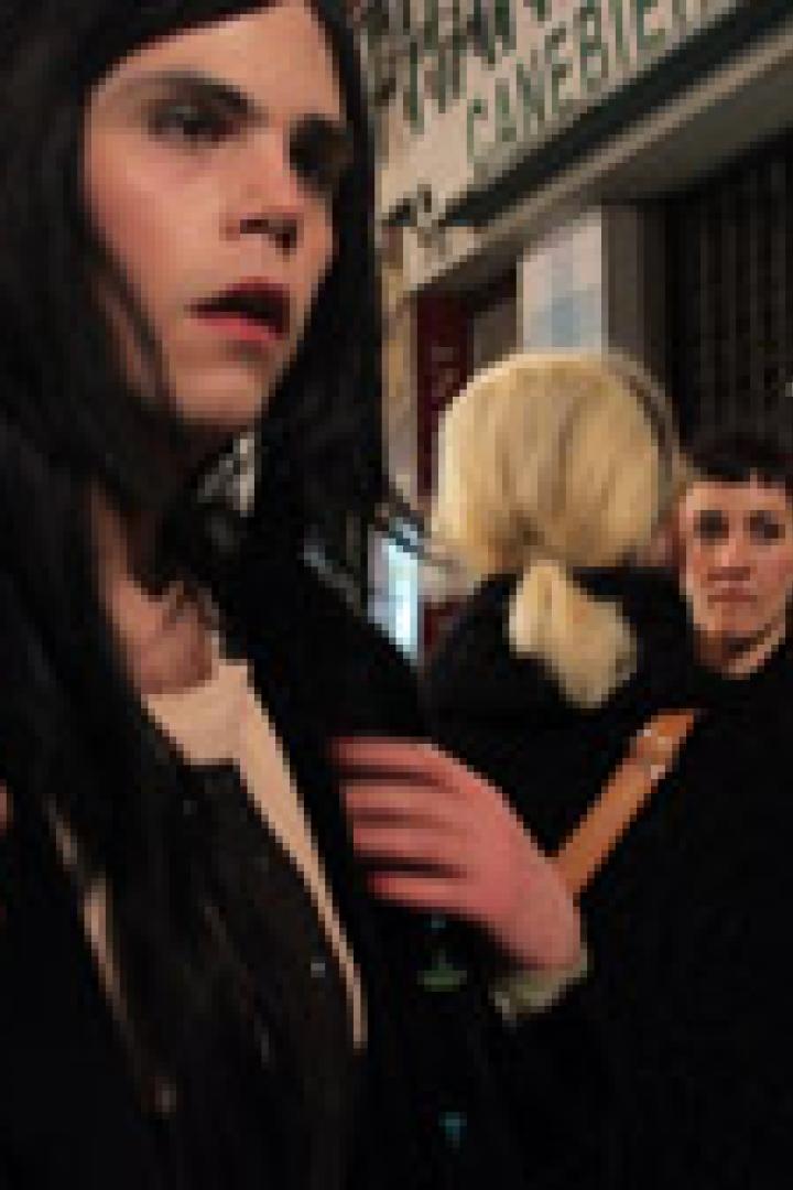 Ein junger Mann mit dunklen, langen Haaren und dunkler Jacke steht nachts auf der Straße.