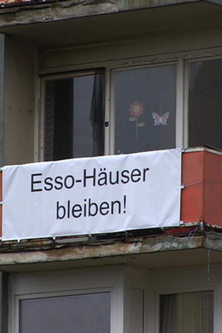 An einem Wohnhaus hängt ein Banner mit der Aufschrift „Esso-Häuser bleiben!“.