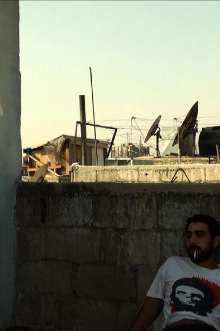 Ein Mann mit Che-Guevara-T-Shirt raucht auf einer Dachterrasse mit arabischer Graffiti im Hintergrund.