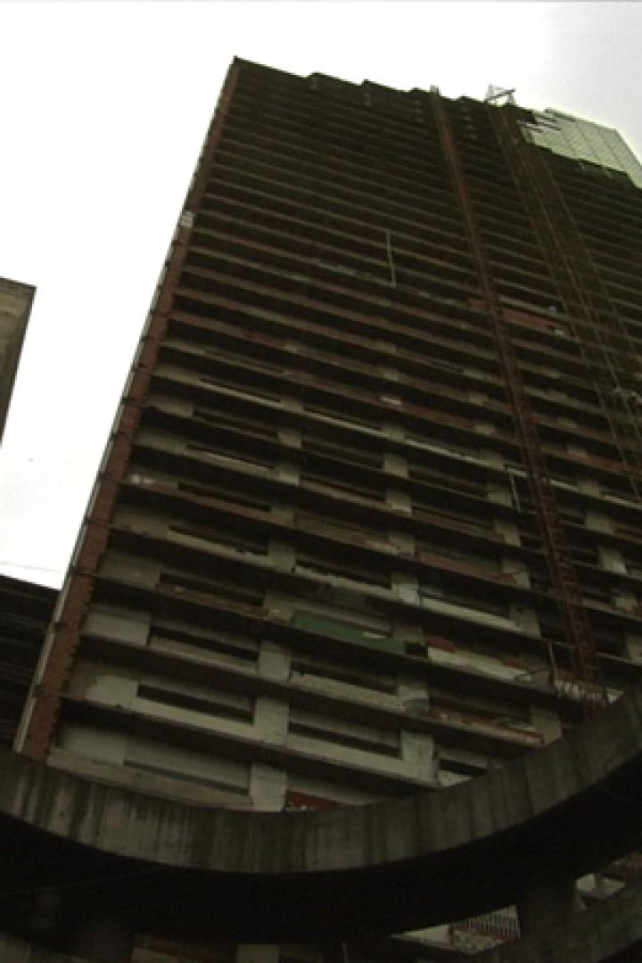 Ein unfertiges Hochhaus wird durch die konzentrischen Kreise einer Betonstruktur hindurch betrachtet.