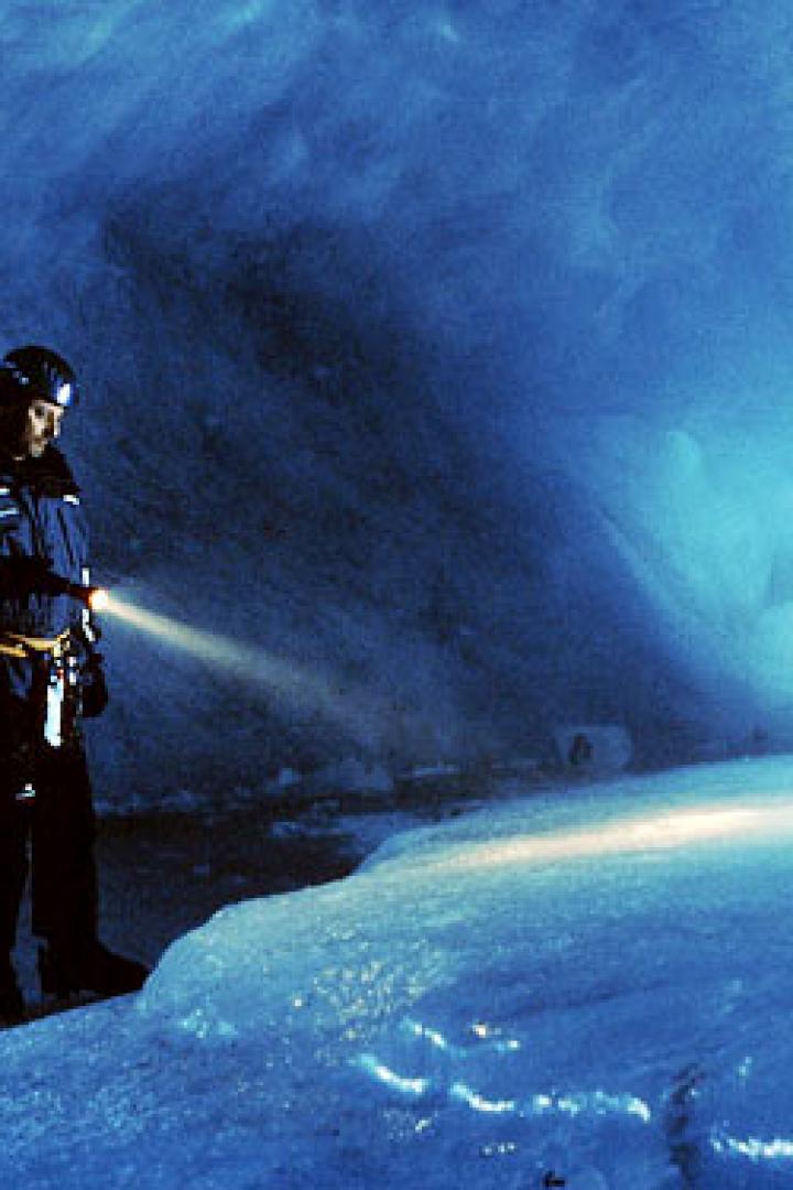 Zwei Personen erkunden eine Eishöhle mit Stirnlampen und einer Taschenlampe.