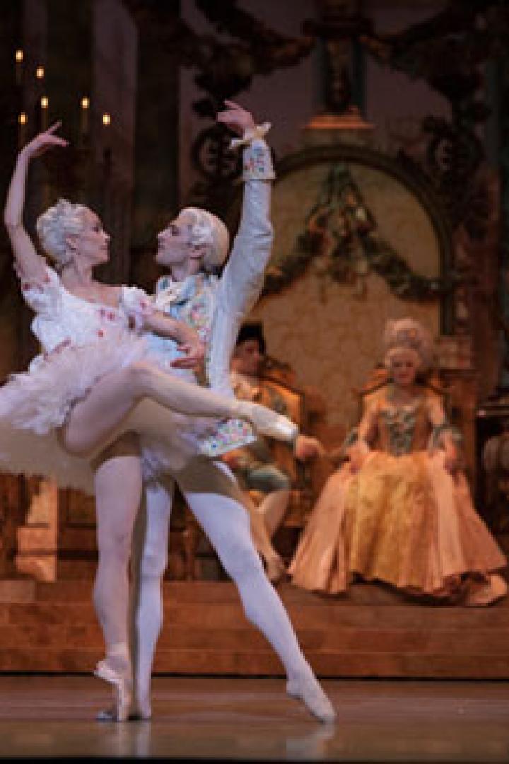 Ein Ballettpaar tanzt auf einer Bühne vor einem opulenten Bühnenbild.
