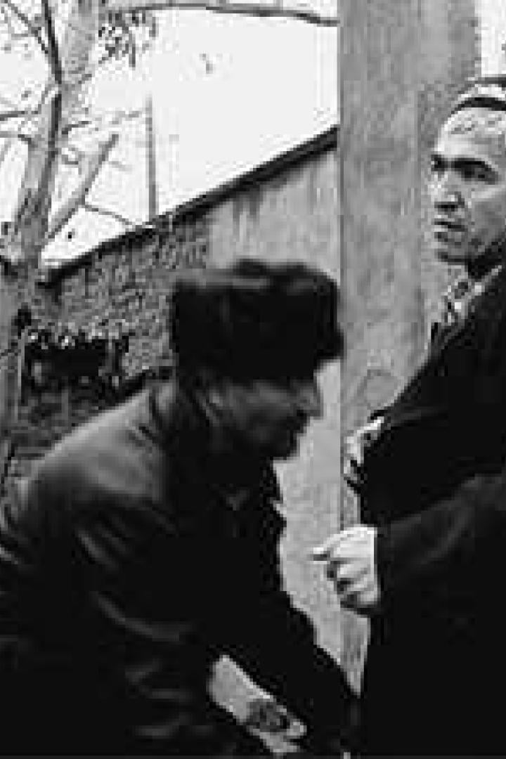 Zwei Männer stehen im Freien, einer mit traditioneller Kopfbedeckung.