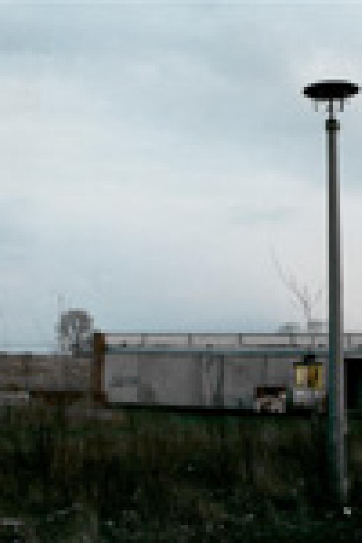 Ein kleines, graues Gebäude steht unter einem bewölkten Himmel neben einer Straßenlaterne.