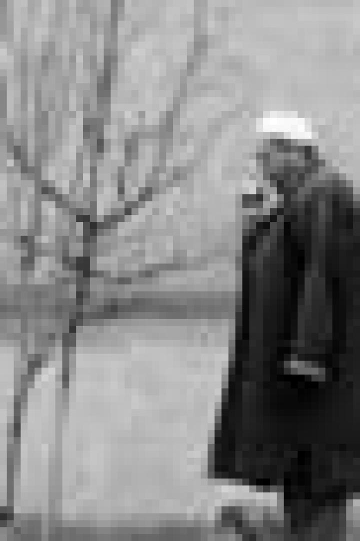 Ein älterer Mann mit Mantel und Mütze steht draußen und raucht.