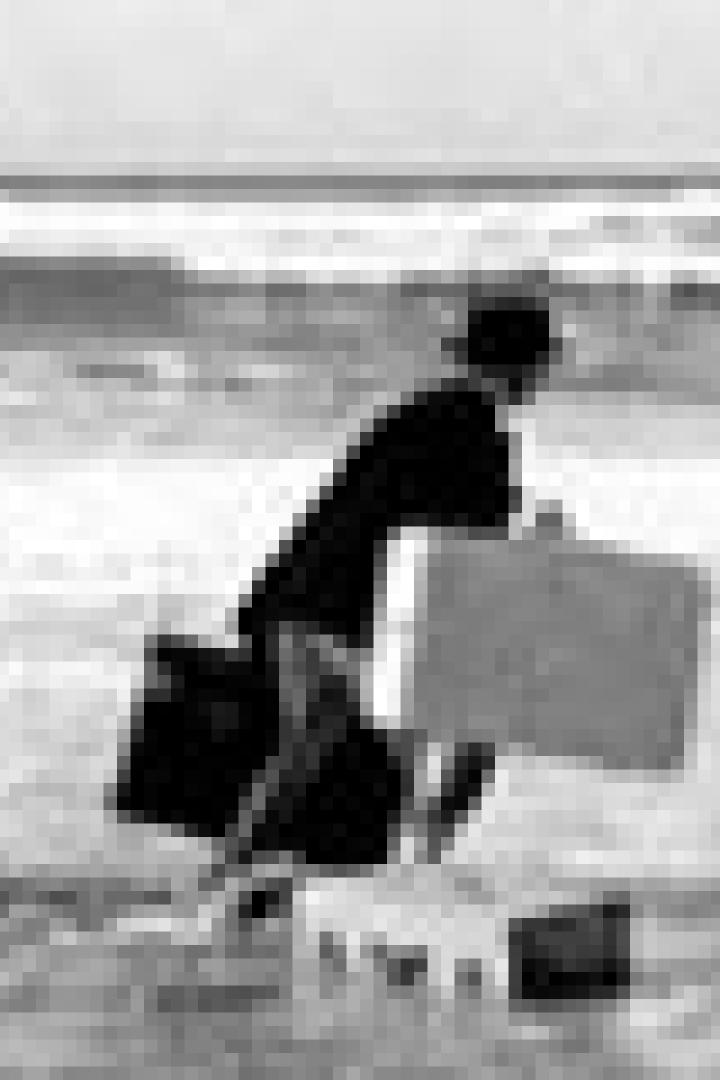 Ein Mann mit Anzug und Hut rennt mit Koffern am Strand entlang.