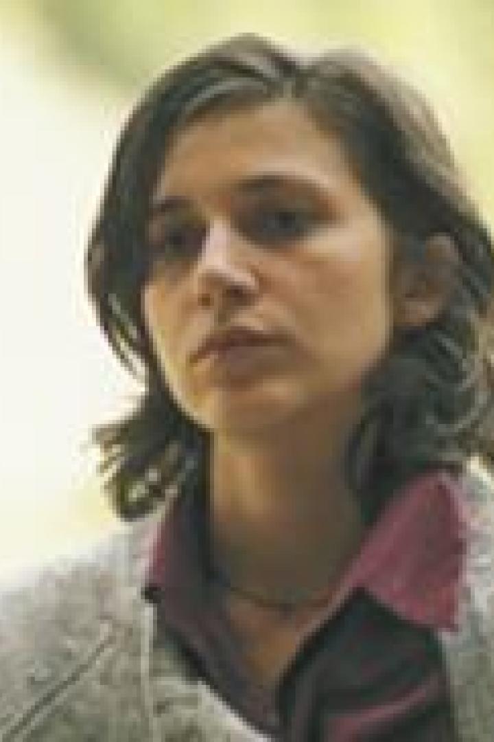 Eine Frau mit dunklen, lockigen Haaren und einem ernsten Gesichtsausdruck.