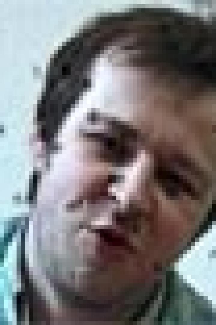 Ein Mann mit kurzem, dunklem Haar und einem karierten Hemd schaut in die Kamera.
