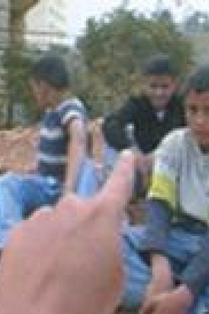 Eine Gruppe von Jungen sitzt auf dem Boden, während ein Finger auf einen von ihnen zeigt.