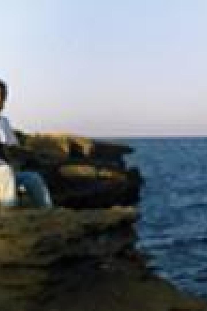 Ein Mann sitzt auf einer Klippe mit Blick auf das Meer.