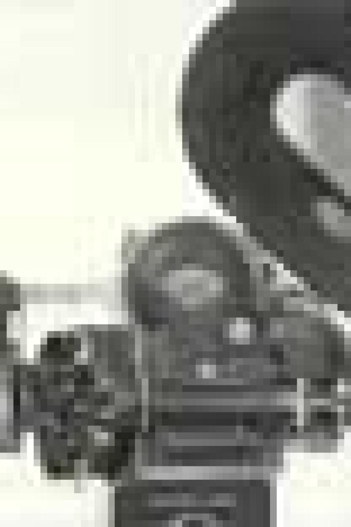 Eine alte Filmkamera mit Gegenlichtblende vor einem hellen Hintergrund.