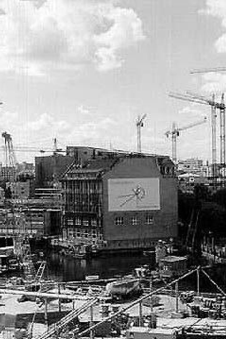 Zahlreiche Baukräne prägen die Skyline einer Stadt am Wasser.