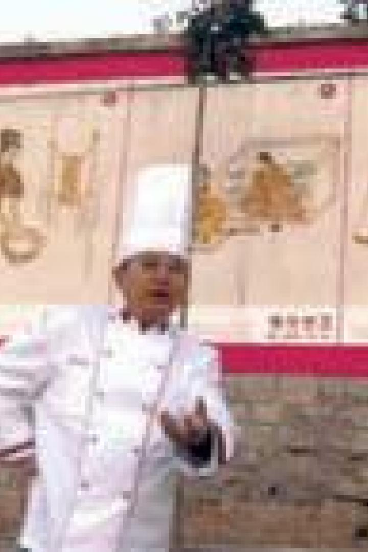 Ein Koch in Kochuniform steht vor einer Wand mit historischen Malereien.