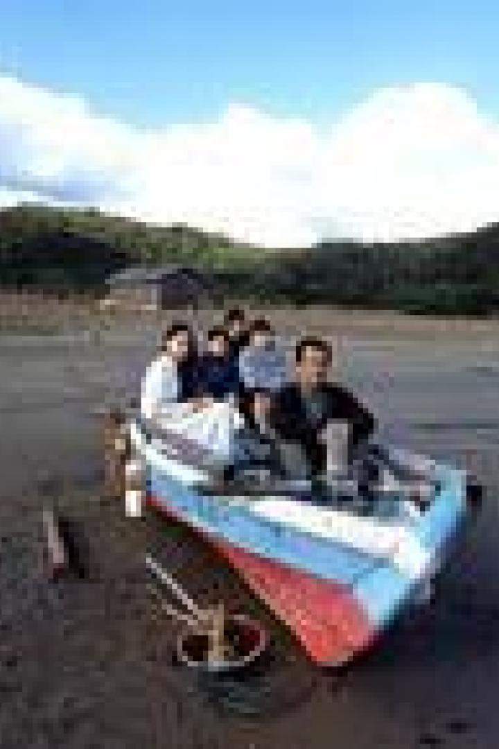 Eine Gruppe von Menschen sitzt in einem bunten Boot am Strand.