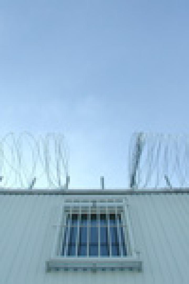 Ein weißes Gebäude mit einem vergitterten Fenster und Stacheldraht unter einem blauen Himmel.