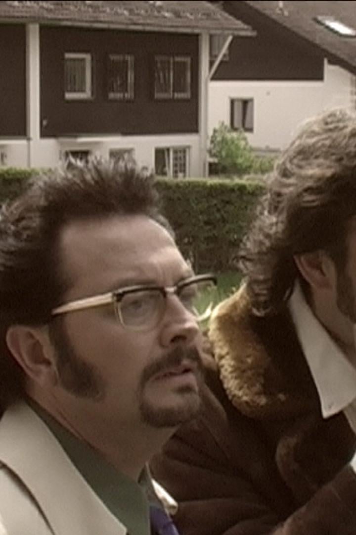 Zwei Männer mit Schnurrbärten und Retro-Kleidung stehen im Freien.