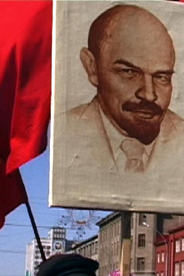 Eine rote Flagge mit Hammer und Sichel und ein Porträt von Lenin bei einer Demonstration.