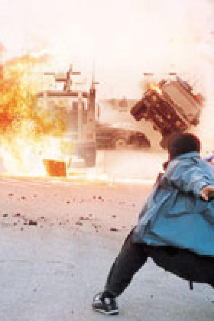 Ein Mann wirft einen Gegenstand auf ein Auto, das explodiert.