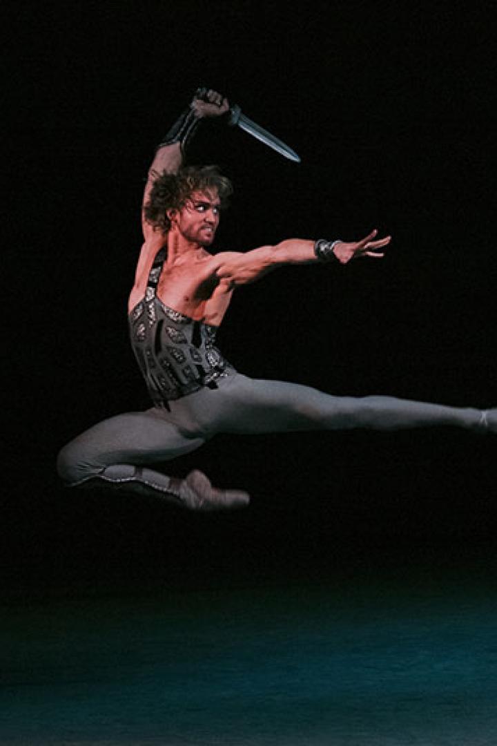 Ein männlicher Ballettänzer springt mit einem Dolch in der Hand auf der Bühne.