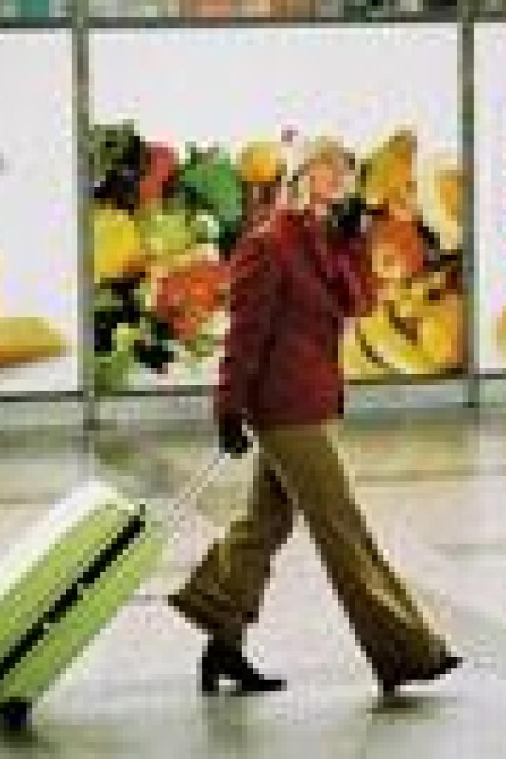 Eine Frau zieht einen Rollkoffer vor Werbeplakaten her.