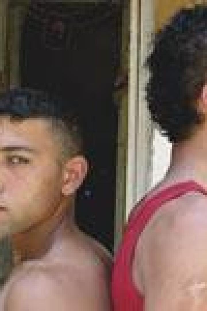 Zwei junge Männer stehen Rücken an Rücken, einer raucht eine Zigarette.