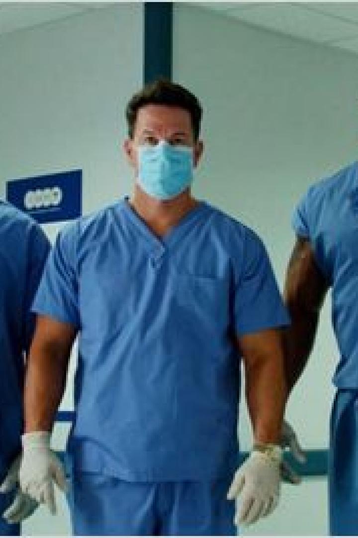 Drei Männer in Arztkleidung stehen in einem Krankenhausflur.