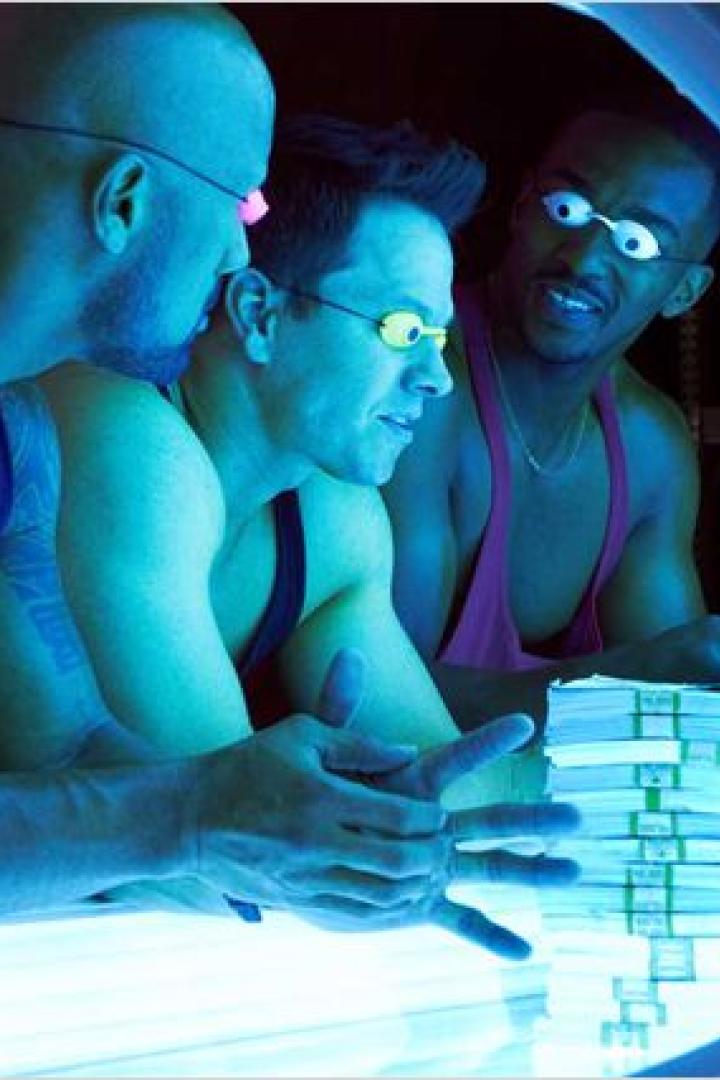 Drei Männer mit Schutzbrillen stehen neben Stapeln von Banknoten.