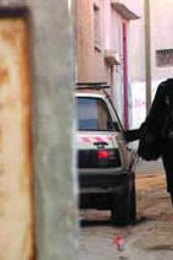 Eine Frau geht eine enge Gasse entlang, im Hintergrund ein geparktes Auto.