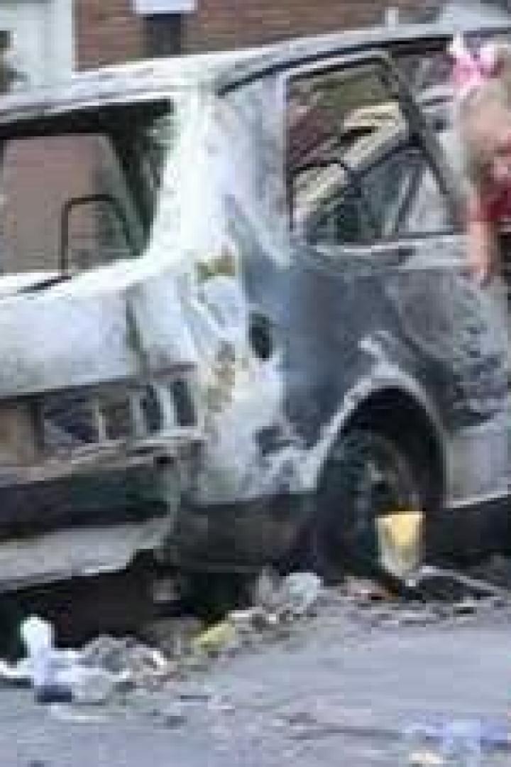 Ein Mädchen kehrt Trümmer vor einem ausgebrannten Auto.