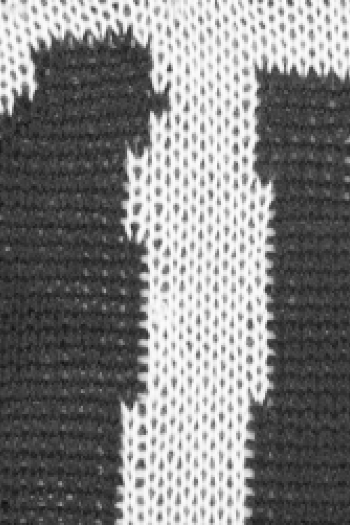 Detailaufnahme eines Strickmusters mit zwei stilisierten, dunklen Figuren auf hellem Grund.