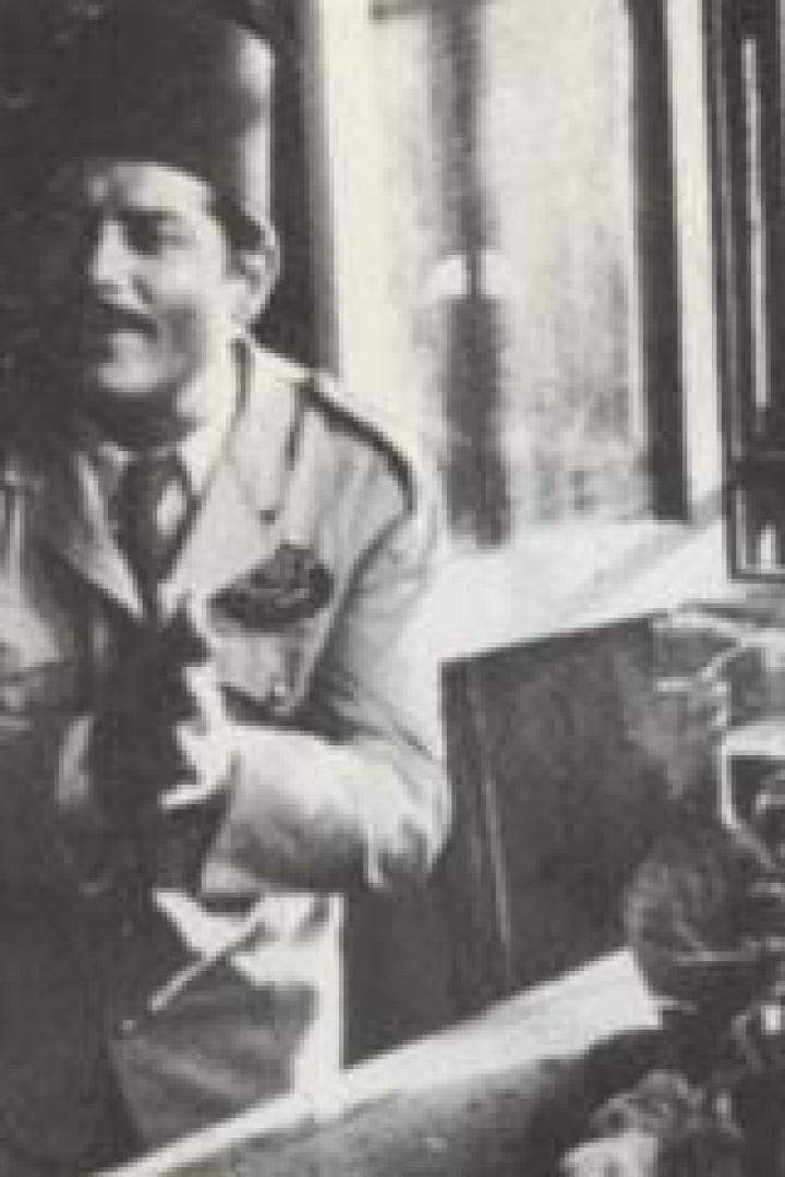 Ein Mann mit Hut und Uniform hält einen Vogel in der Hand, umgeben von Vogelkäfigen.