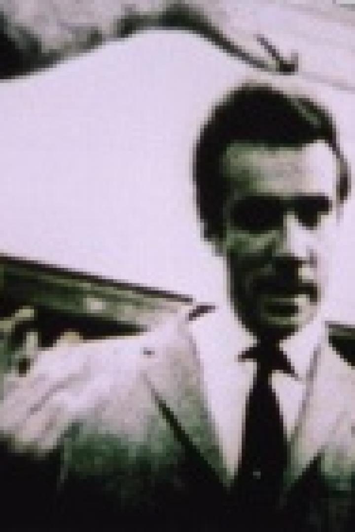 Ein Mann in Anzug und Krawatte gestikuliert vor einer Wand.