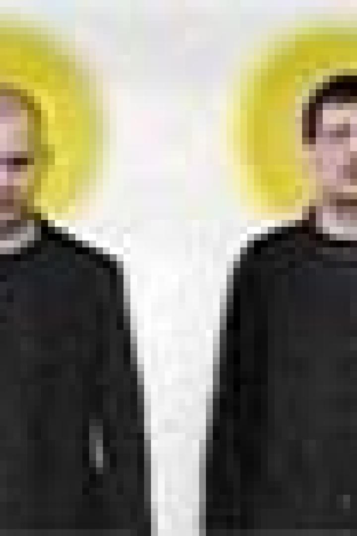 Zwei Männer in schwarzen Hemden stehen nebeneinander vor einem weißen Hintergrund mit gelben Kreisen hinter ihren Köpfen.